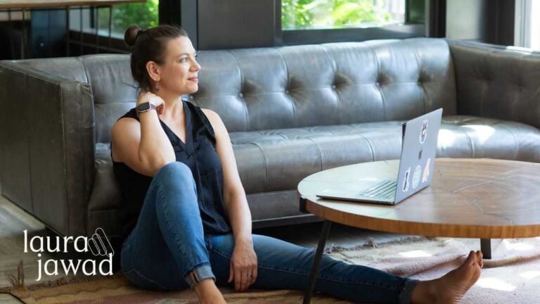 Photo of Laura Jawad sitting on the floor leaning against a couch and looking off into the distance.