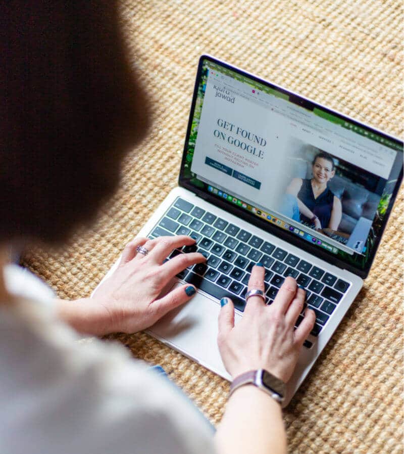 Photo of a laptop taken over someone's shoulder. Laura Jawad's homepage is visible with "get found on google" text prominent.